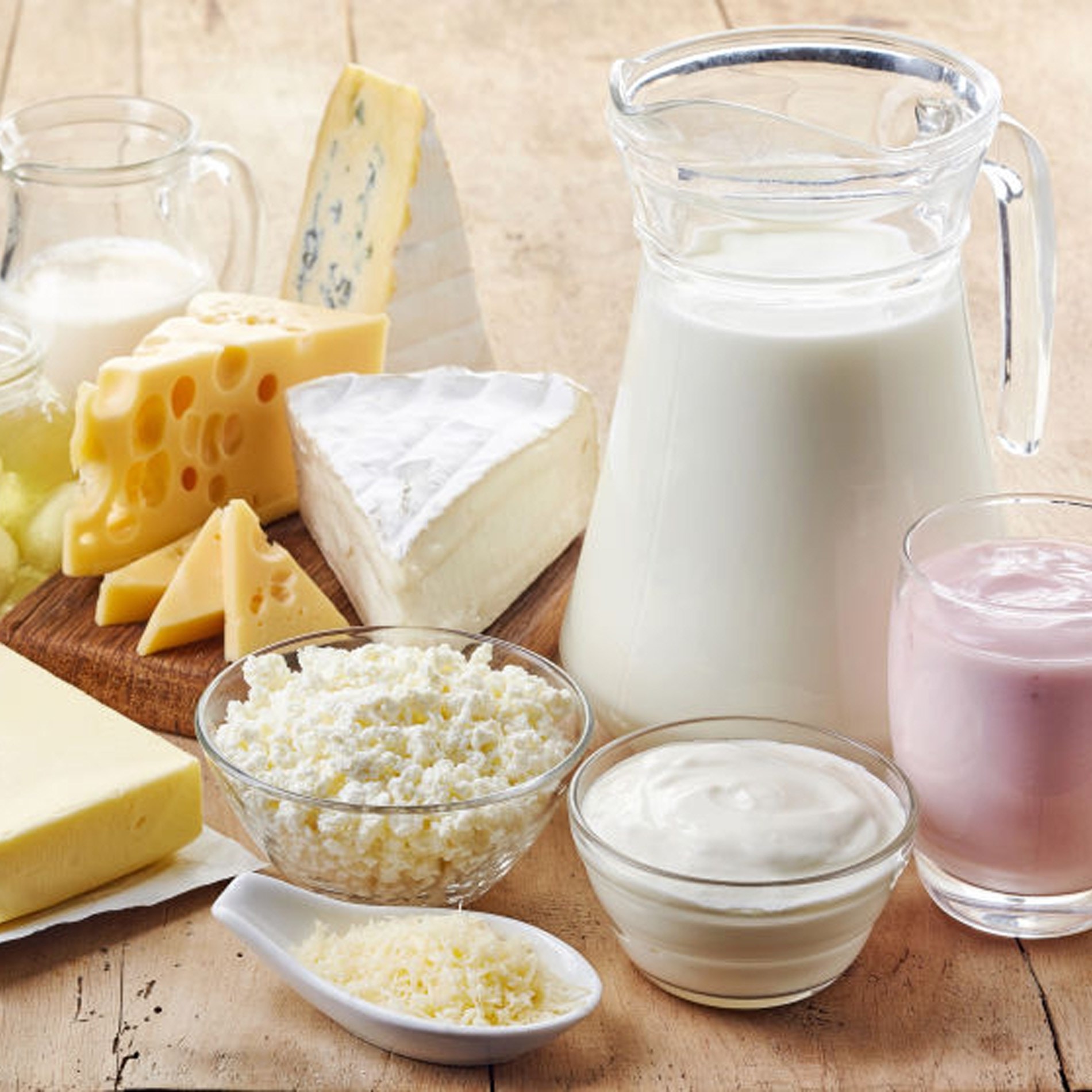 Assorted dairy products on a wooden table, including milk, cheese, yogurt, butter, and cream, arranged in various containers and dishes.