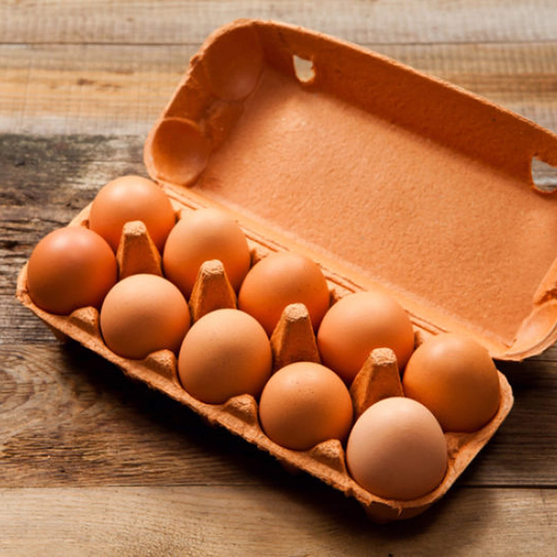 A dozen brown eggs in an open cardboard carton on a wooden surface.