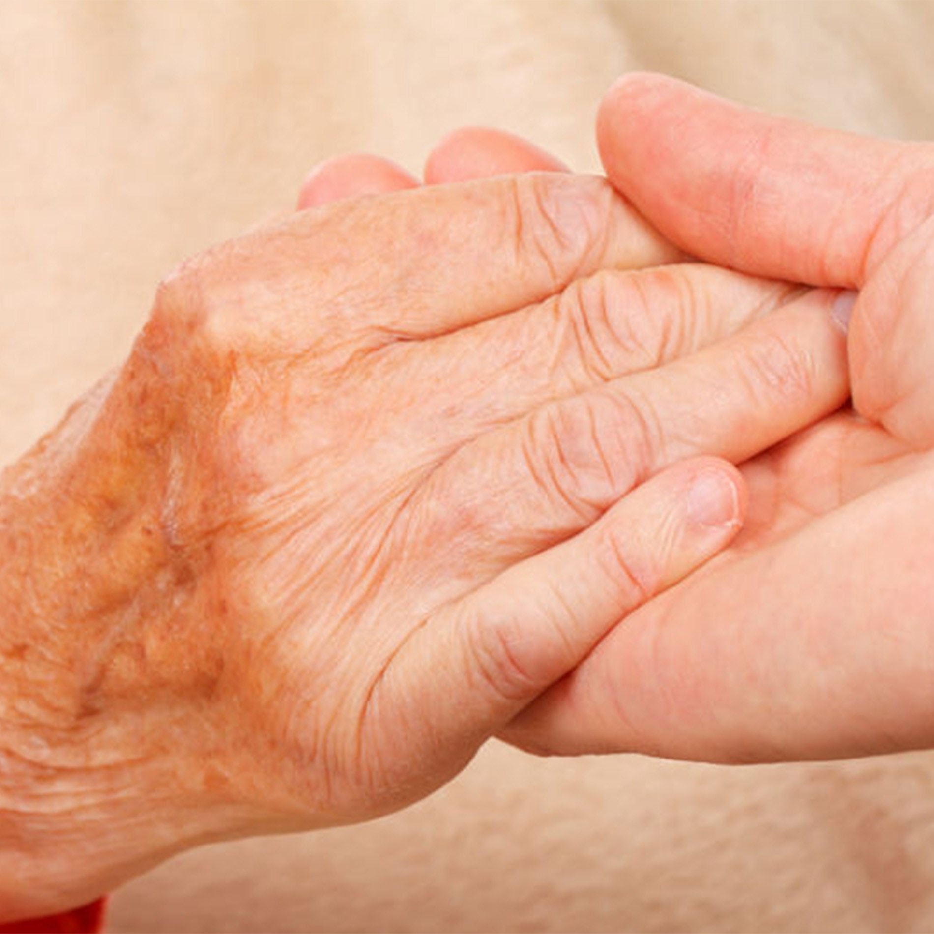 An elderly hand with age spots is gently held by a younger hand, symbolizing care and support.