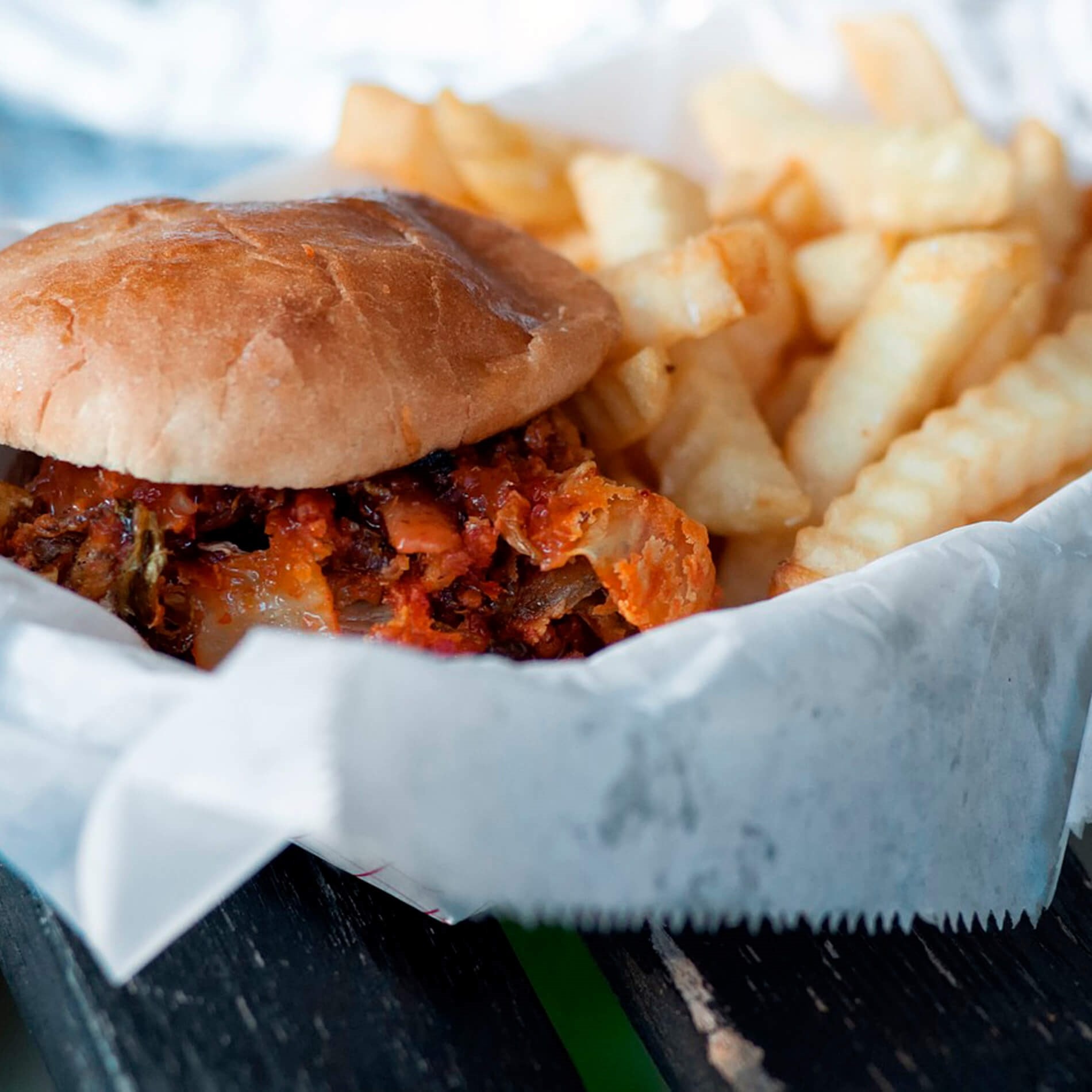 A pulled pork sandwich with barbecue sauce served with crinkle-cut fries on a paper-lined tray.