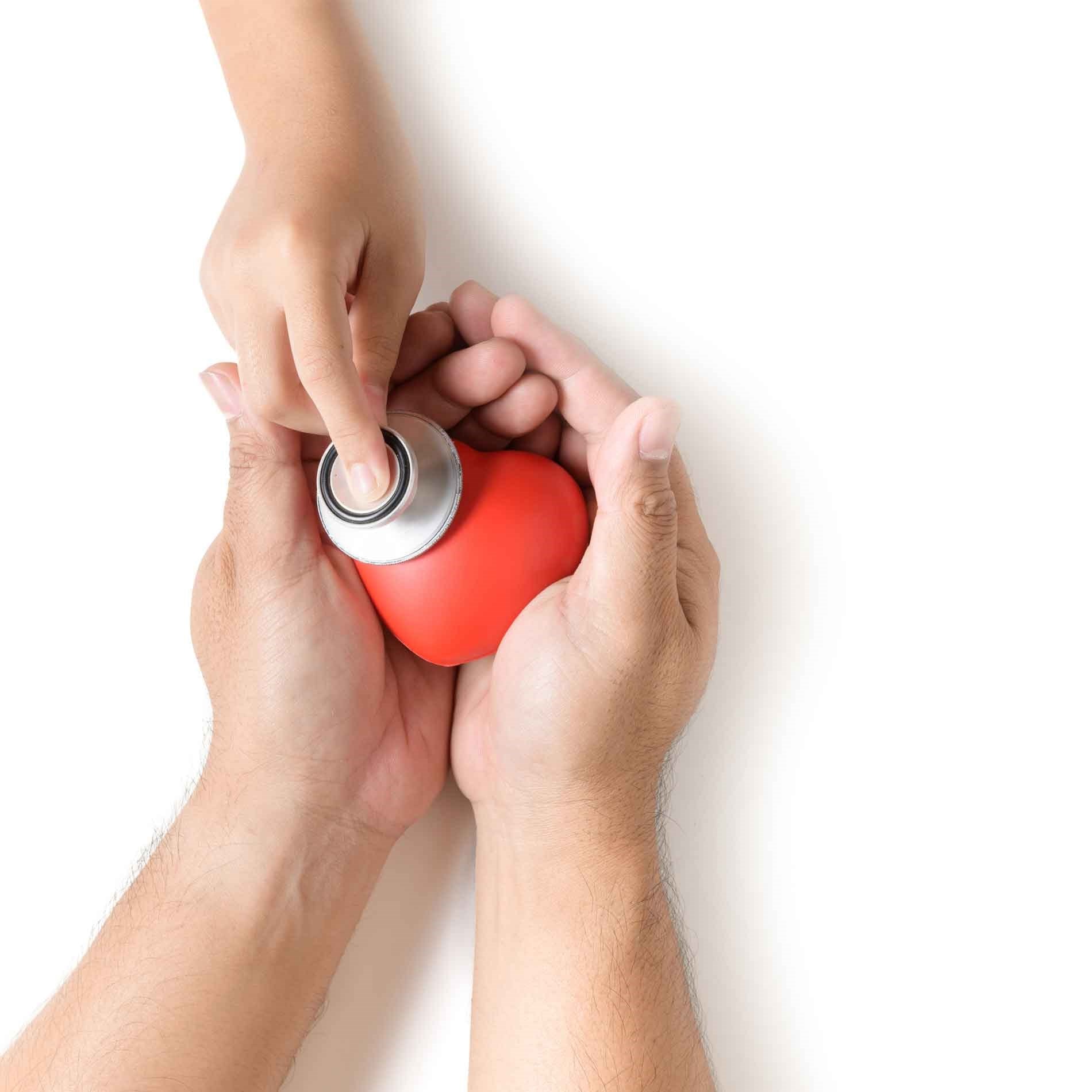 Adult hands hold a red heart while a child's hand uses a stethoscope on it, symbolizing care and health.