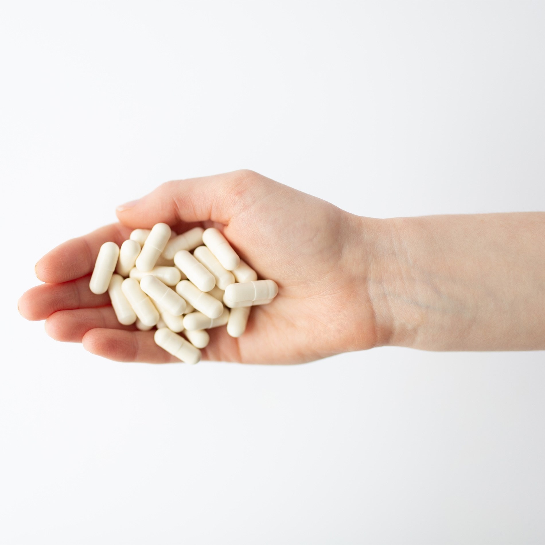 A hand holding several white capsules against a plain white background.