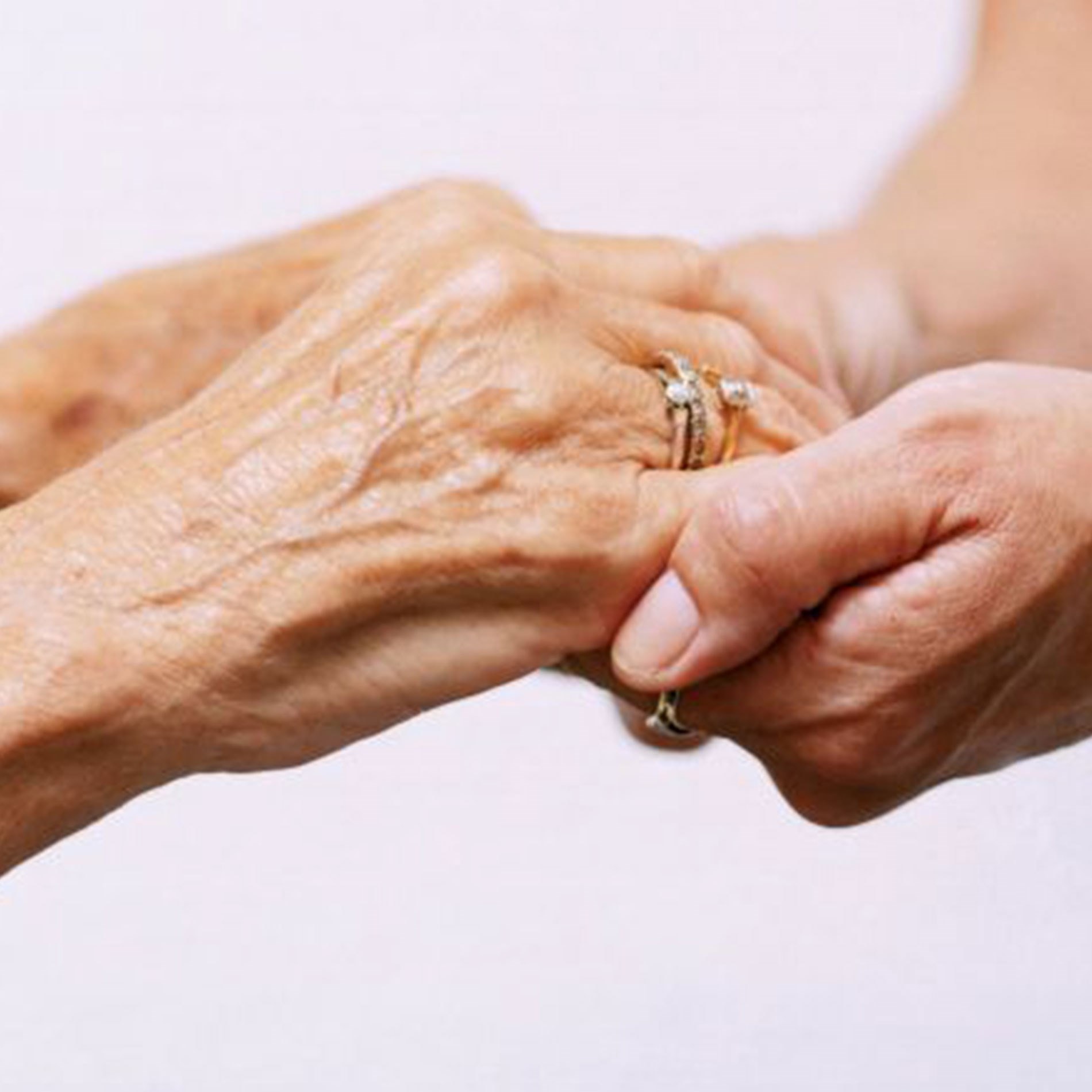 Two hands gently holding each other; one appears older with visible wrinkles, the other younger, symbolizing care and support.