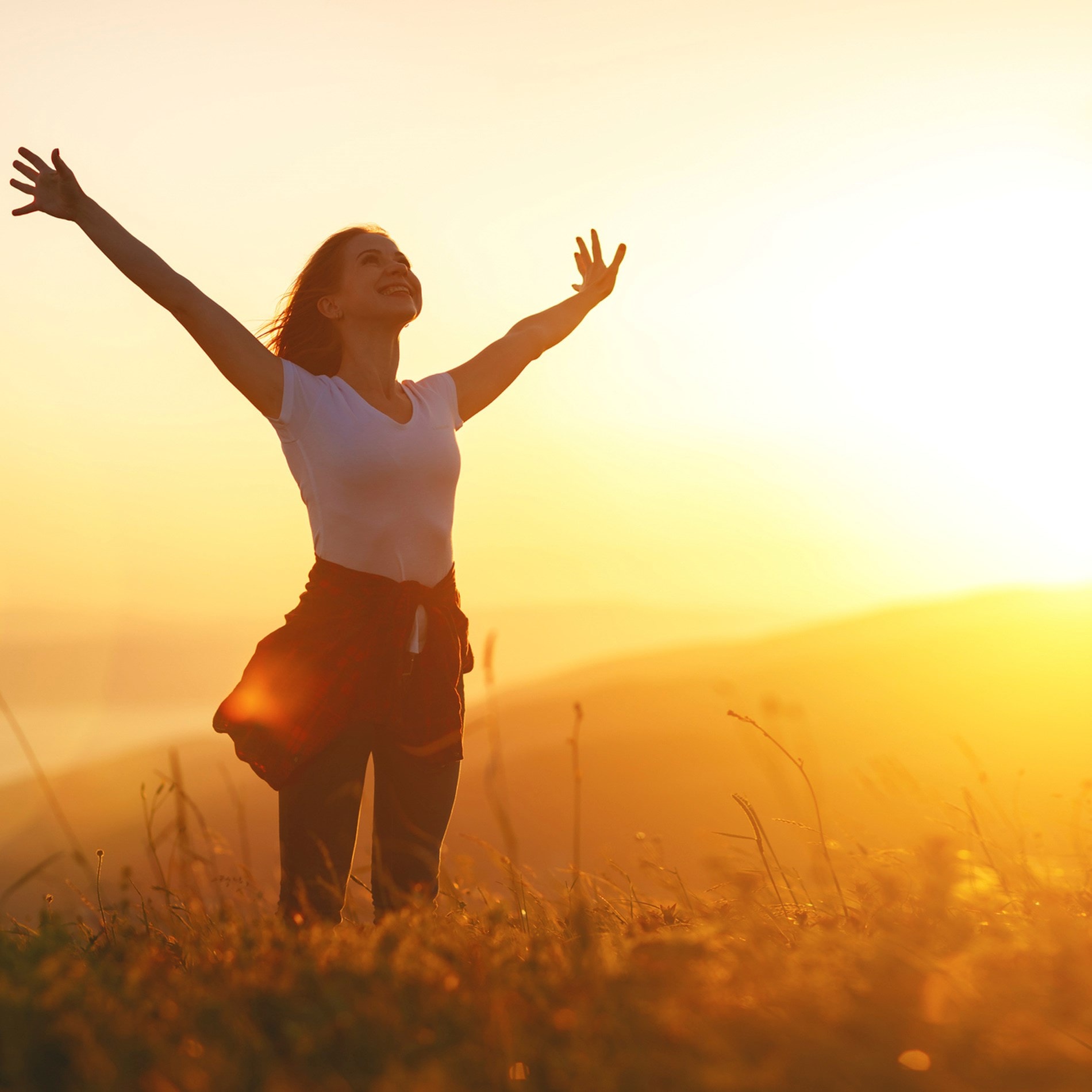 A person stands in a field at sunrise, arms outstretched, embracing the warm light and peaceful scenery.