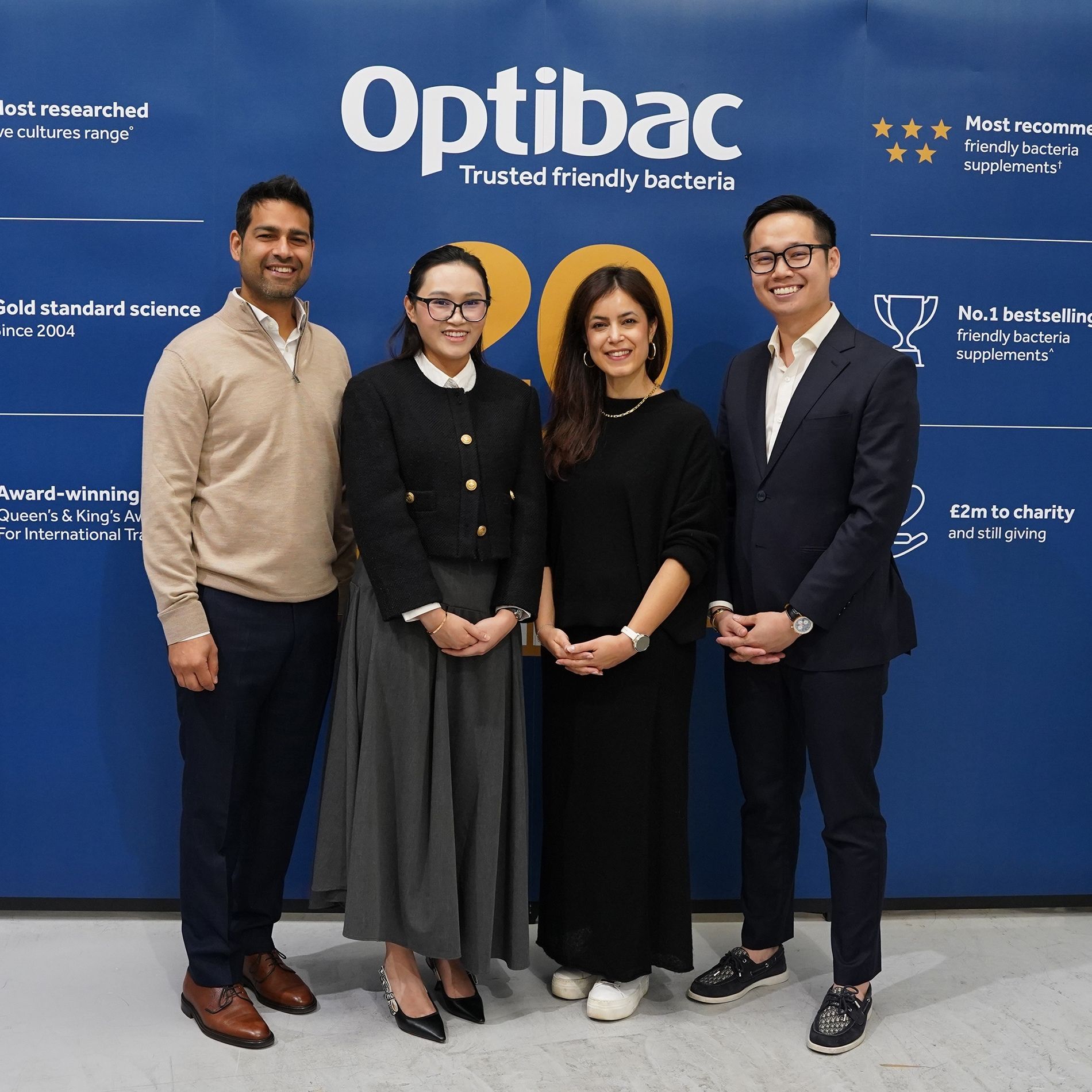 Four people smiling in front of a blue Optibac backdrop with text about the company’s achievements.