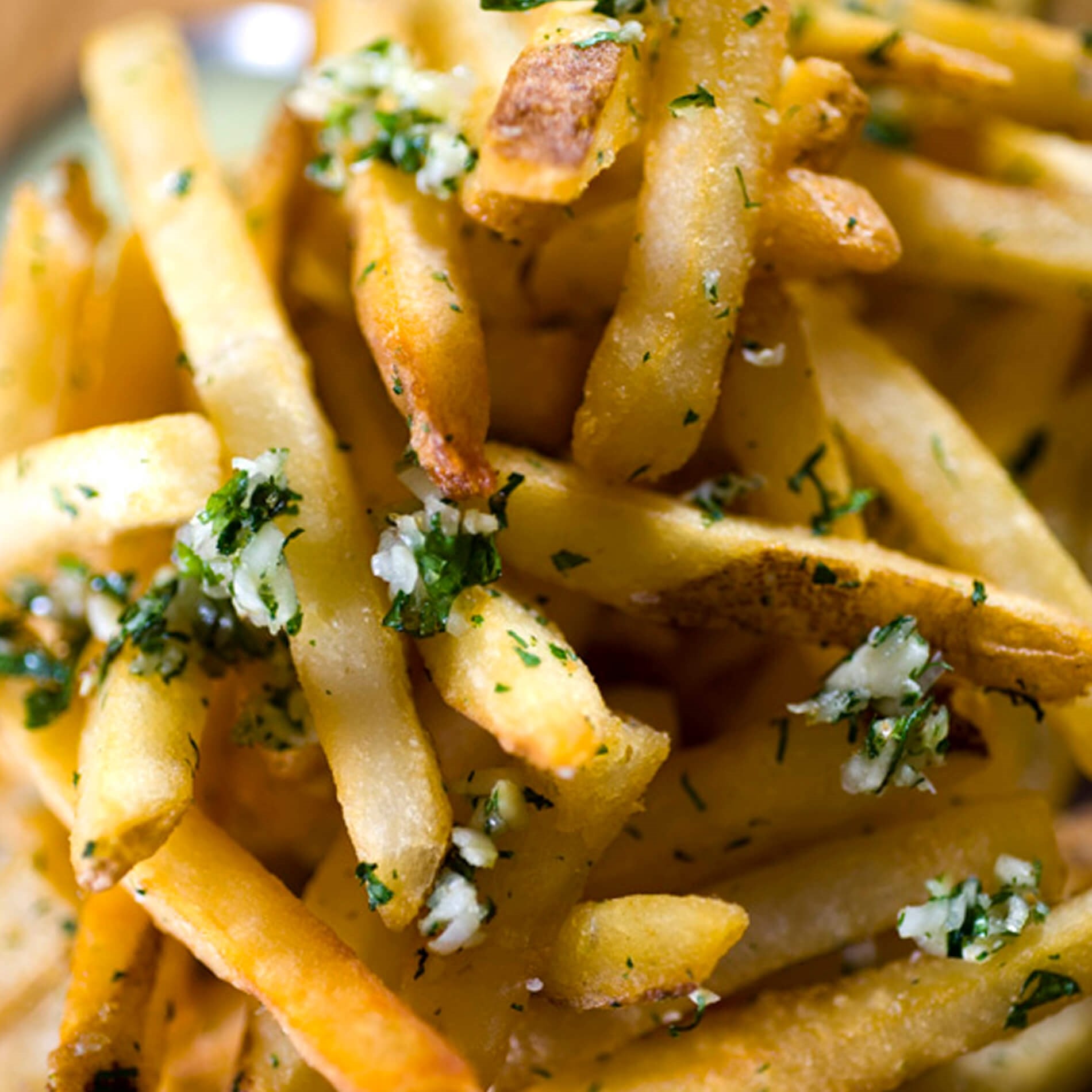 Close-up of golden French fries topped with chopped herbs and minced garlic, showcasing a crispy texture and savory seasoning.