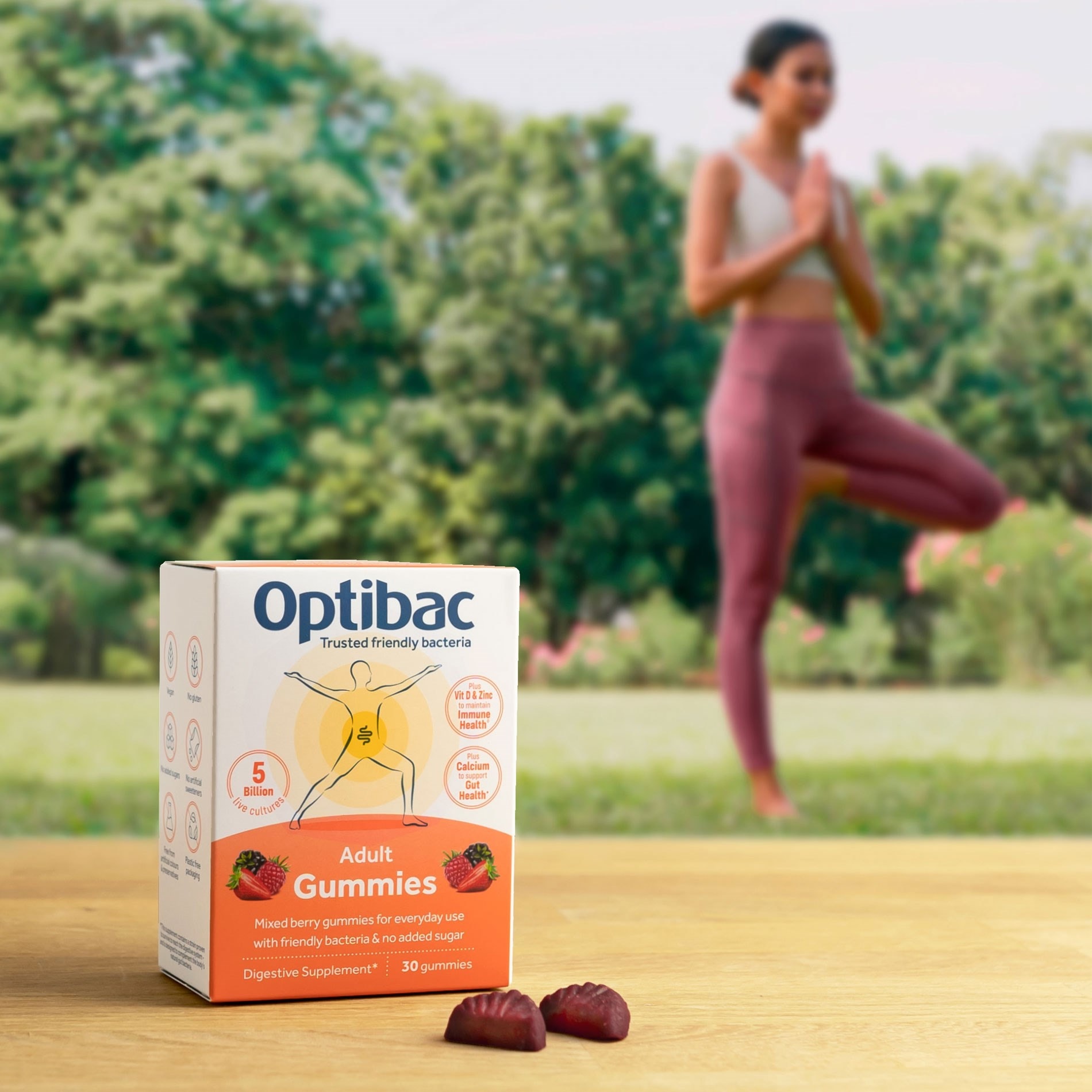 Box of Optibac Adult Gummies on a table, with a woman practicing yoga in the background.