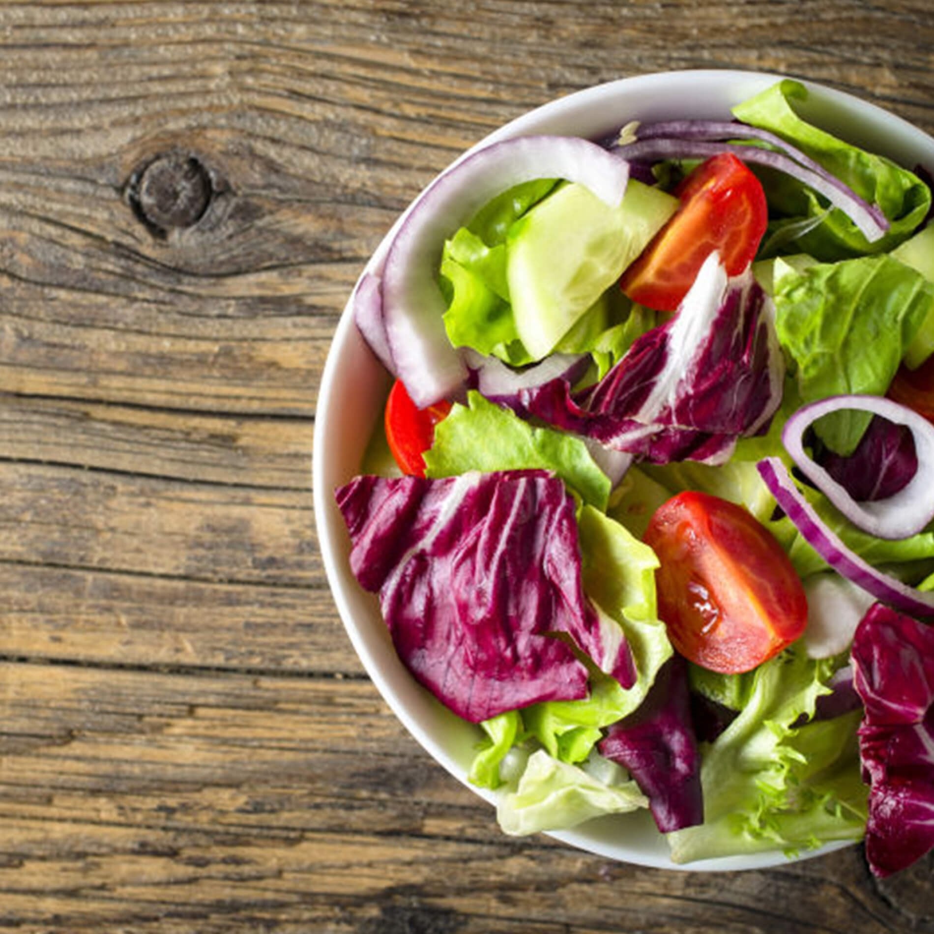 A bowl of fresh salad with lettuce, cherry tomatoes, red onion, and radicchio on a wooden table.
