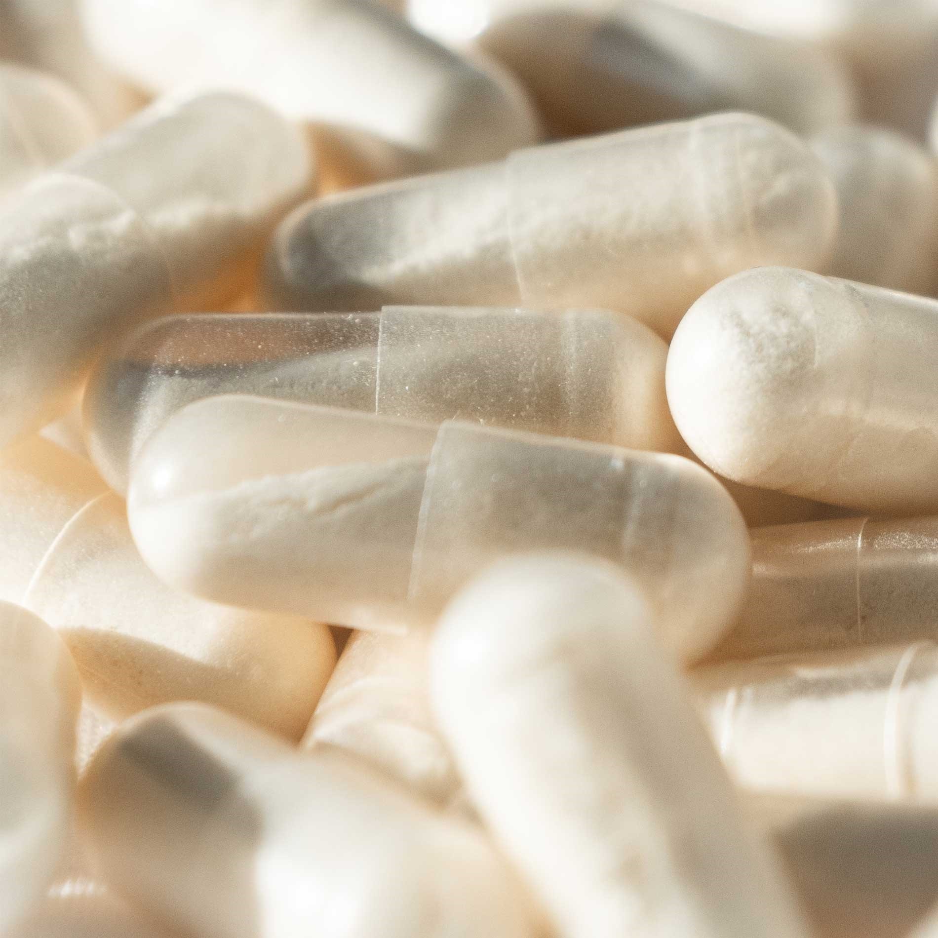 Close-up of translucent, white capsules piled together, with a soft focus highlighting their smooth, glossy surfaces.