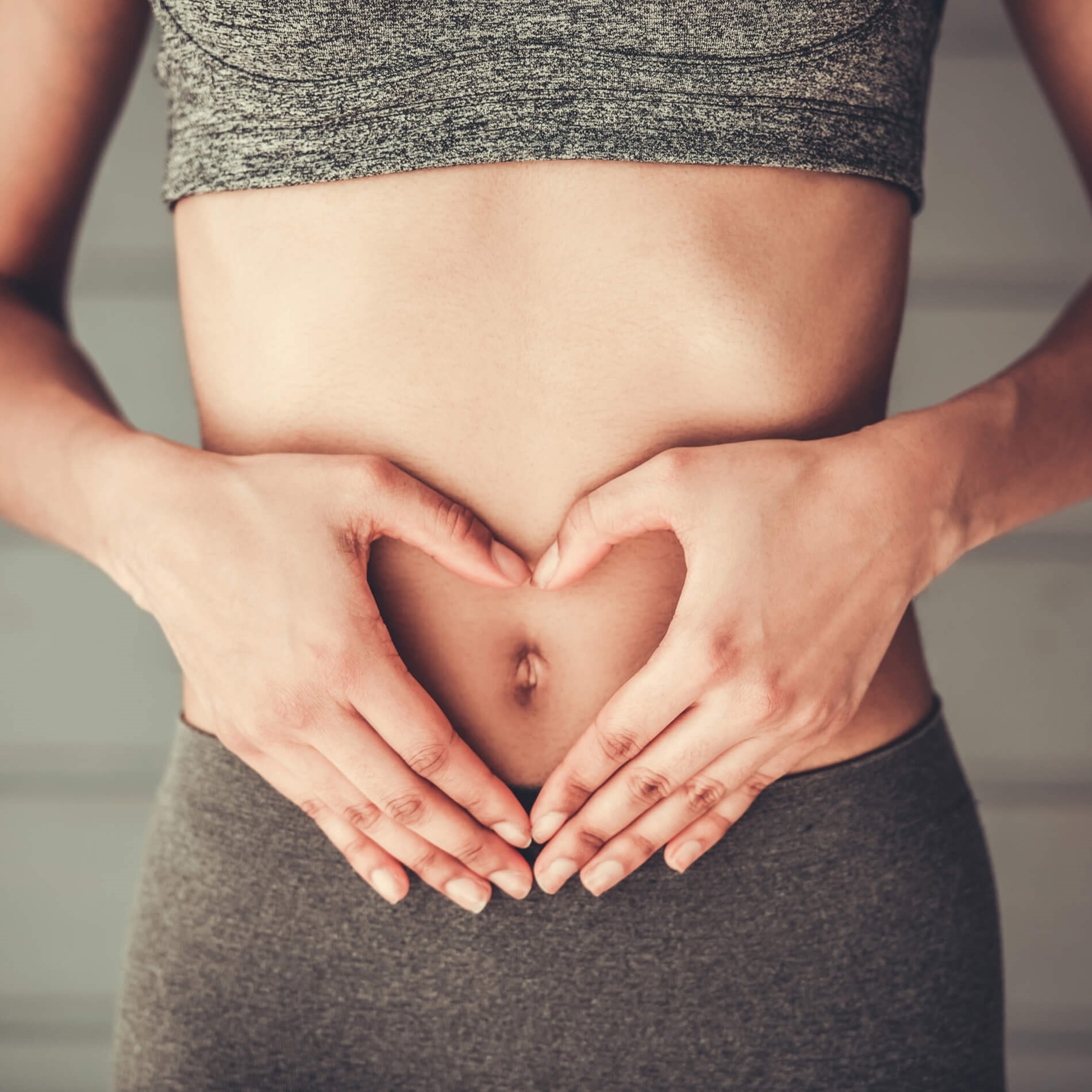 Person in gray workout attire forming a heart shape with hands over their stomach, symbolizing health and wellness.