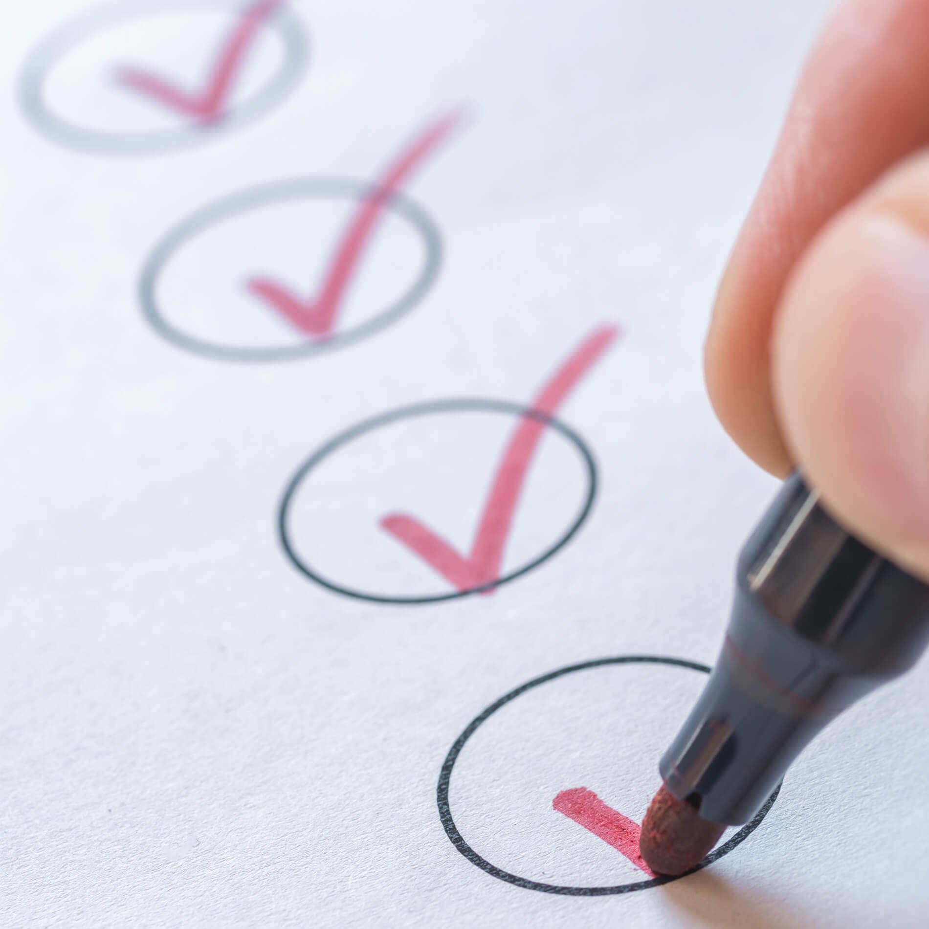 A hand using a red marker to check off items in a list of circles on paper.