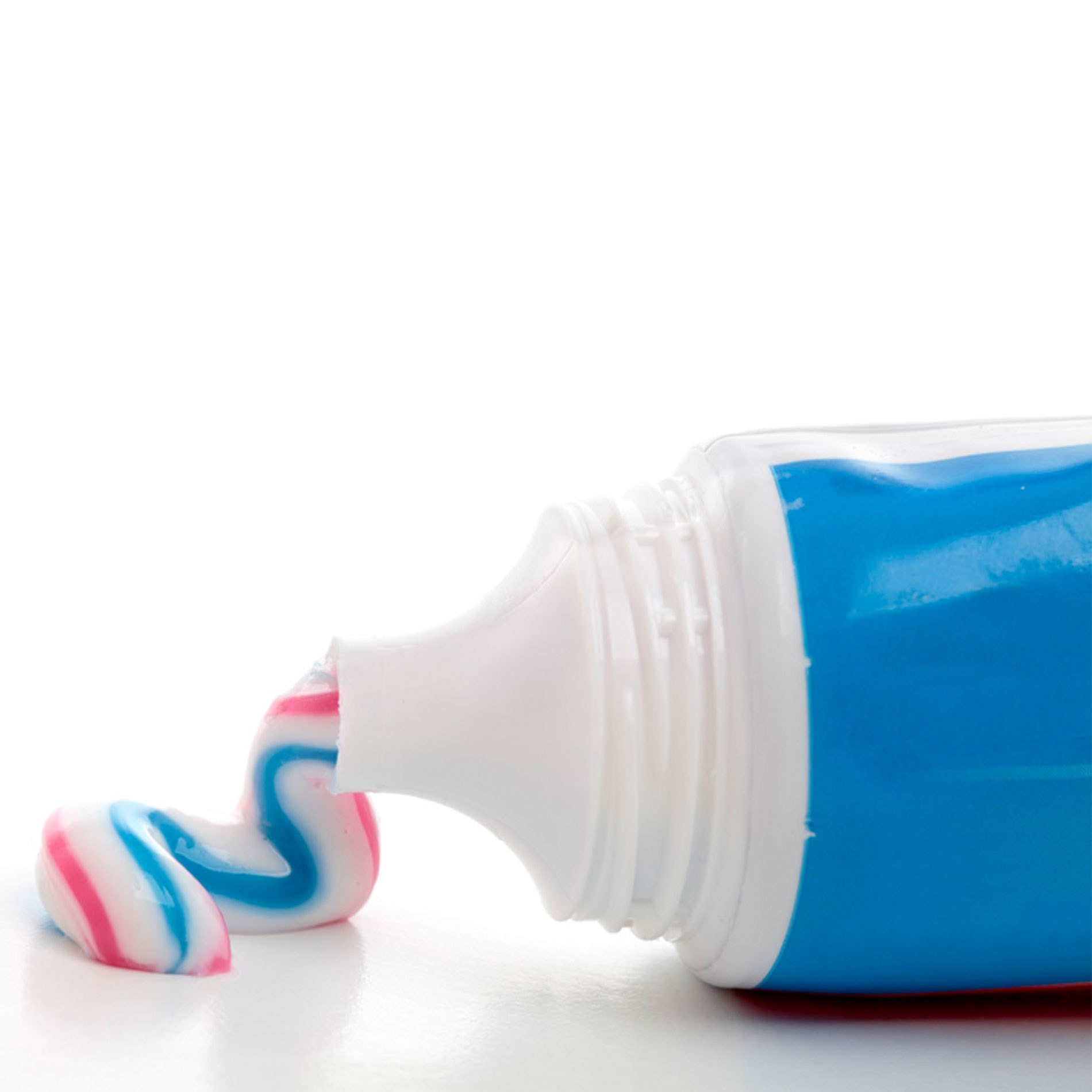 A tube of toothpaste with blue, white, and pink stripes squeezed out onto a white surface.