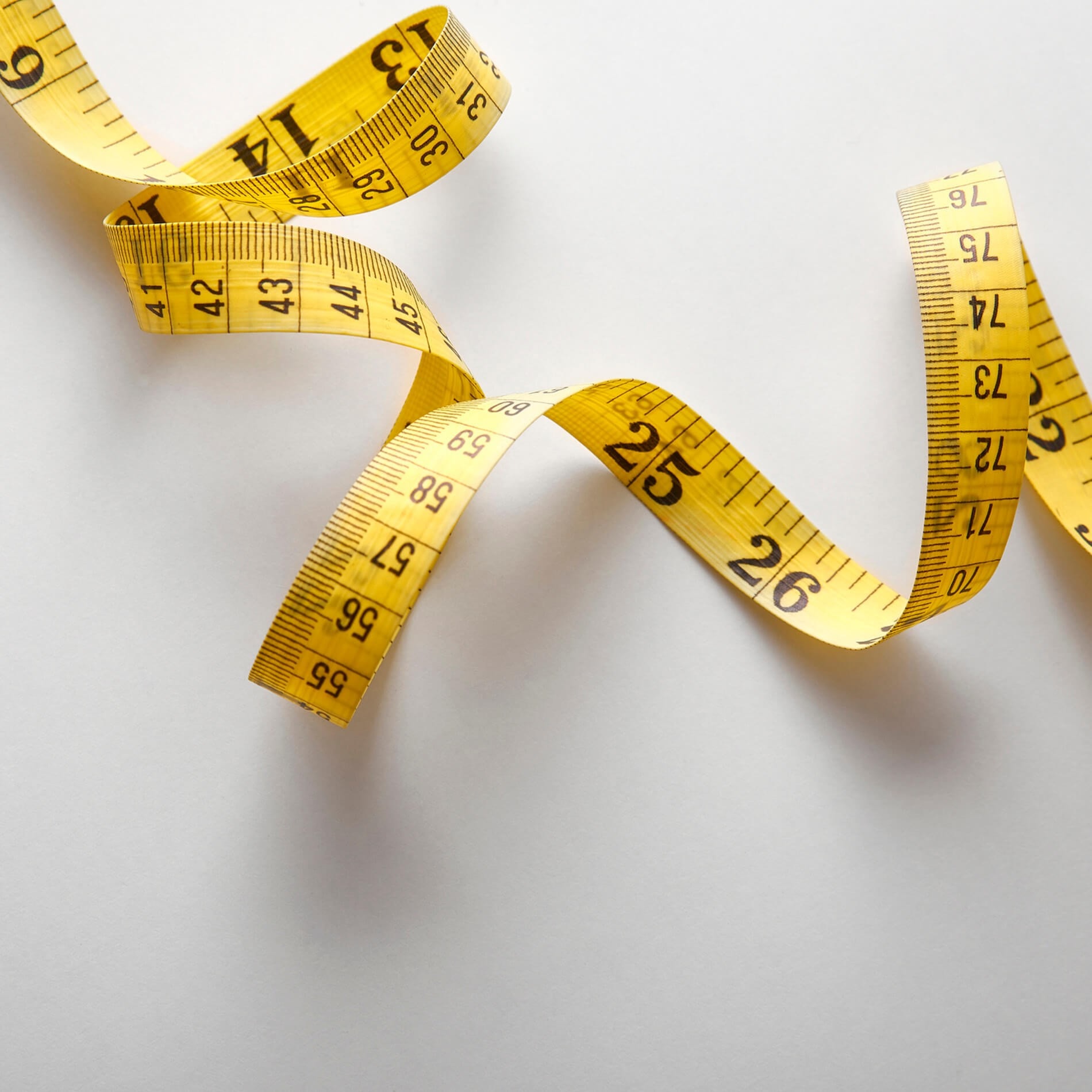 Yellow measuring tape curled on a white surface, displaying both inches and centimeters.