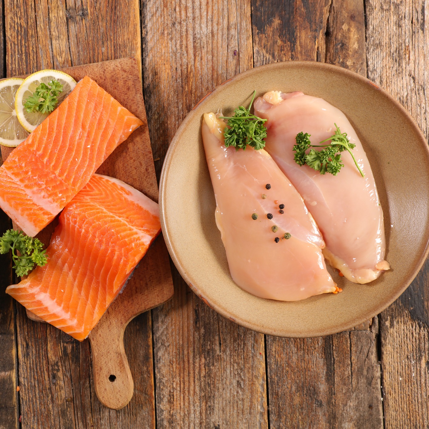 Raw salmon fillets, chicken breasts with herbs, and a carton of eggs on a rustic wooden surface.