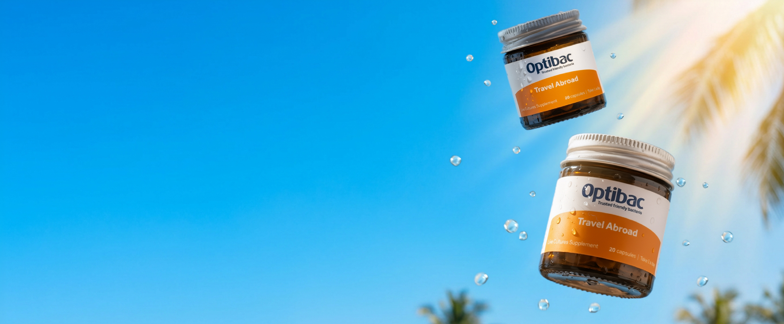 Two Optibac "Travel Abroad" supplement jars with water droplets, set against a blue sky and palm tree background.