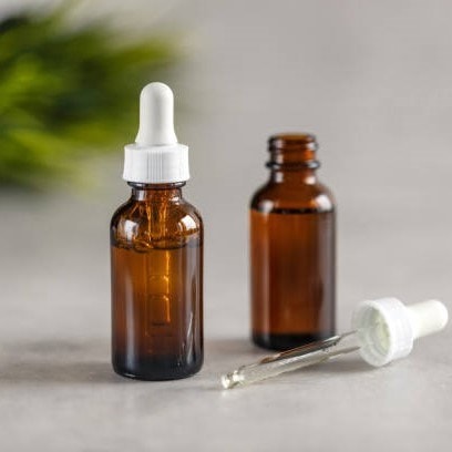 Two amber dropper bottles, one with a dropper beside it, placed on a light surface with blurred greenery in the background.