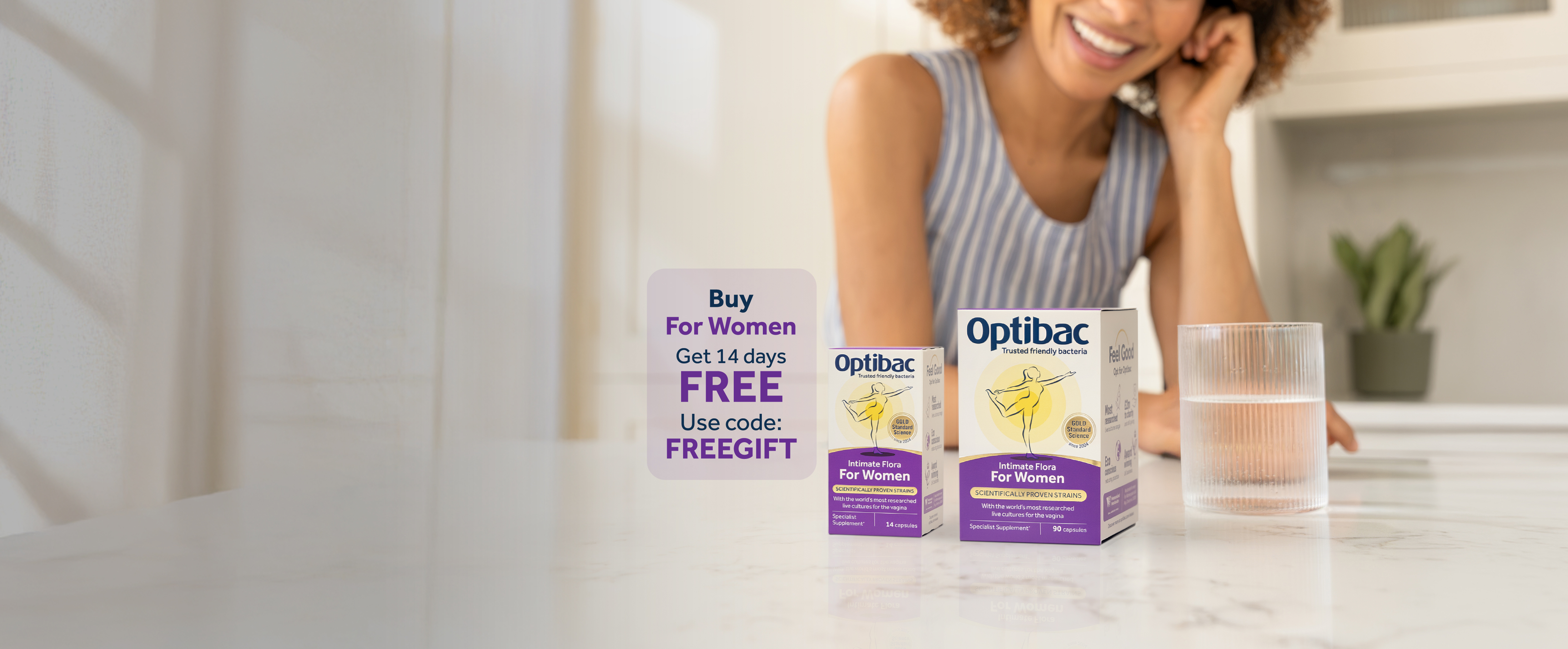 A person smiling at a kitchen table with Optibac probiotic products and a glass of water, promoting a free 14-day offer for women when you buy 30 or 90 capsules.