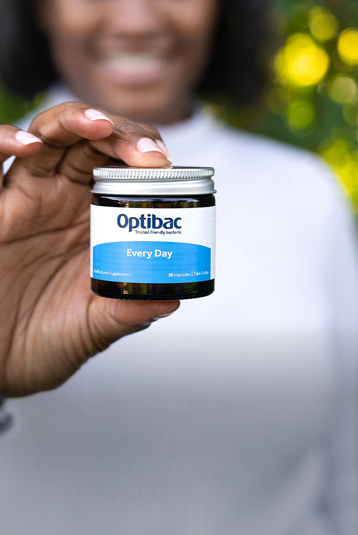 Person holding a small jar of Optibac Every Day capsules, with a blurred green and white background.
