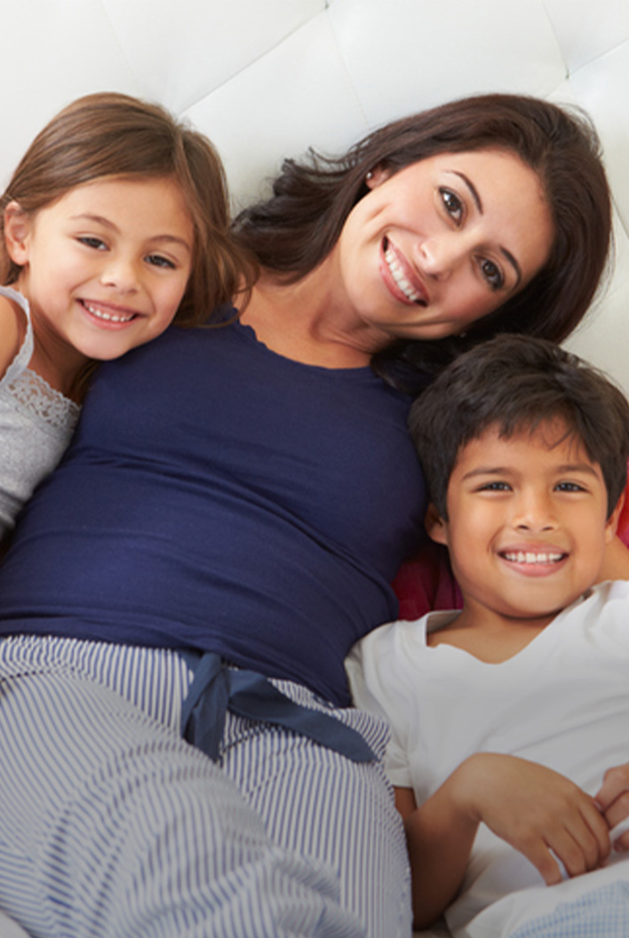A woman and two children, a girl and a boy, smiling while relaxing on a white couch.