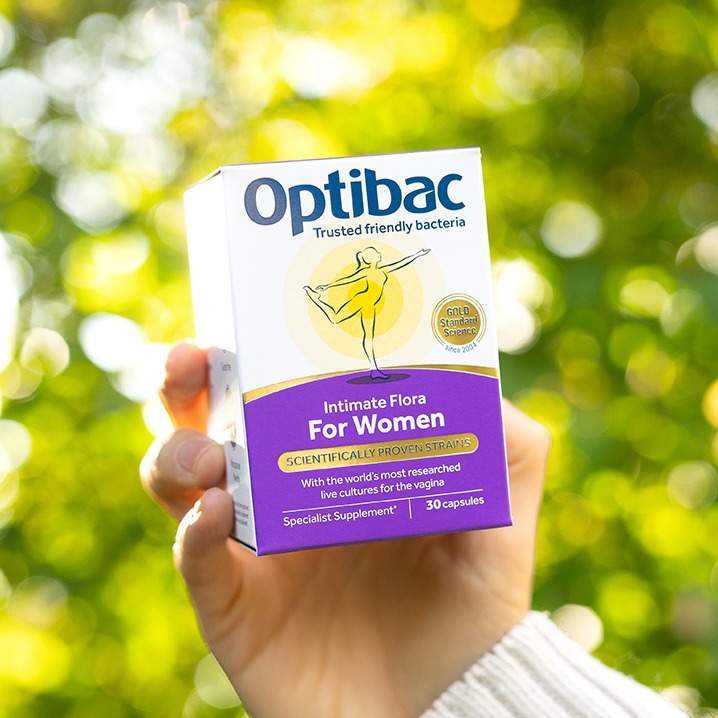 Hand holding a box of Optibac Intimate Flora for Women against a leafy background, showcasing probiotic supplement details.