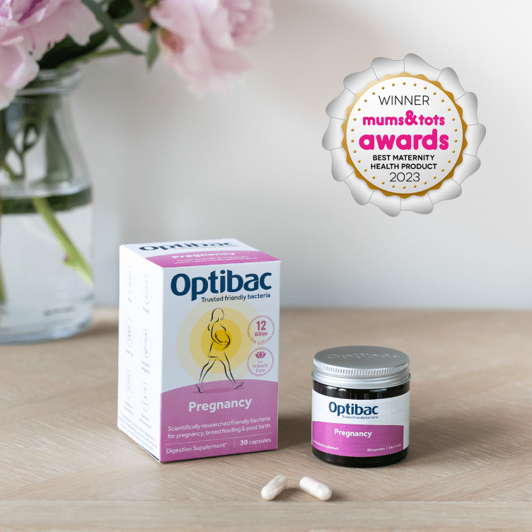 Optibac Pregnancy supplements with award badge, placed on a table beside a pink flower vase. Two capsules are in the foreground.