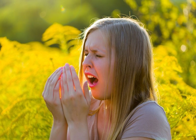 woman sneezing into hands 
