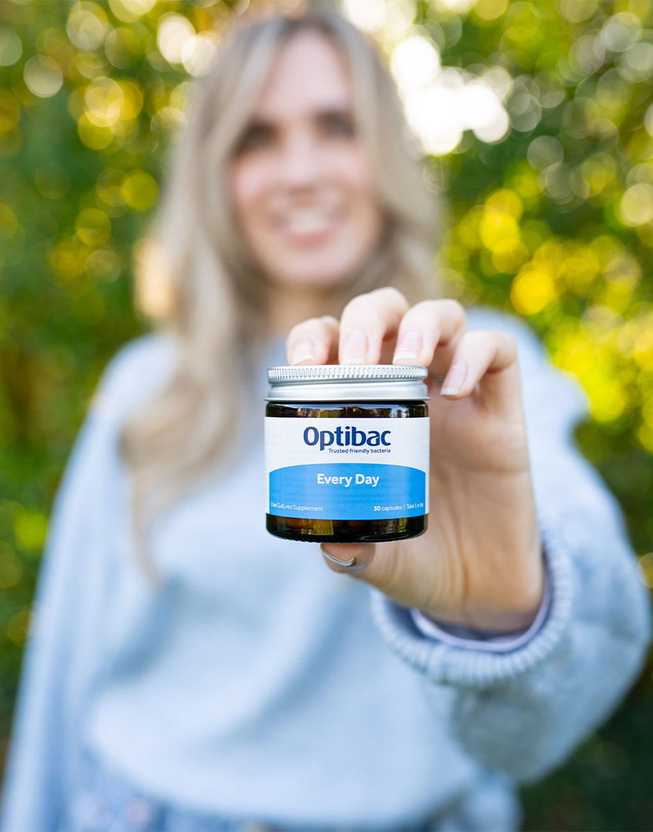 A person holding a jar of Optibac Every Day supplements outdoors, with greenery in the background.