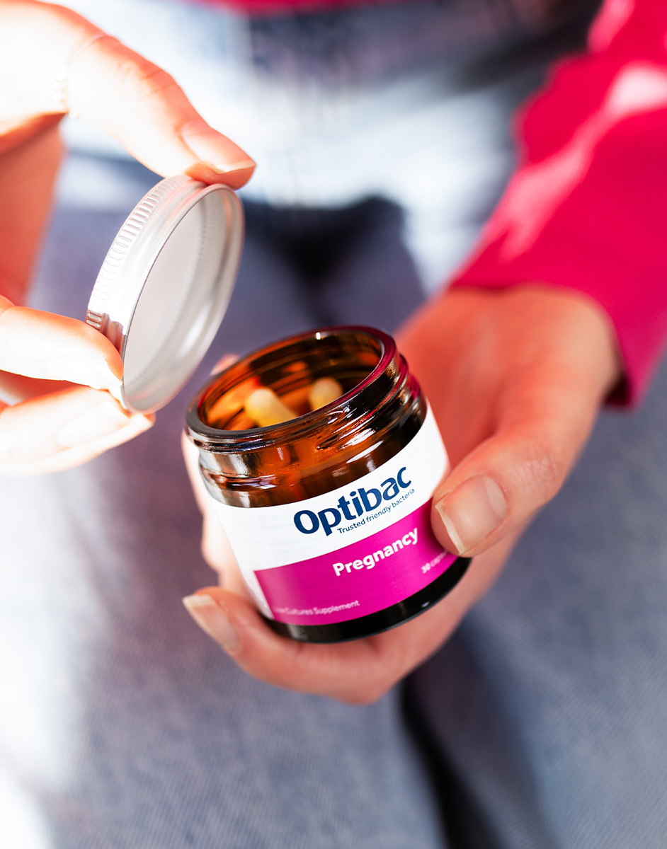 Person opening a jar of Optibac Pregnancy probiotics, with a pink label, while wearing jeans and a pink top.