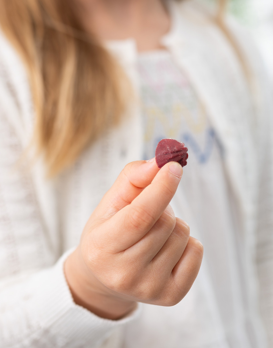 A person with long hair holds a small, red gummy candy shaped like a shell, wearing a white sweater.