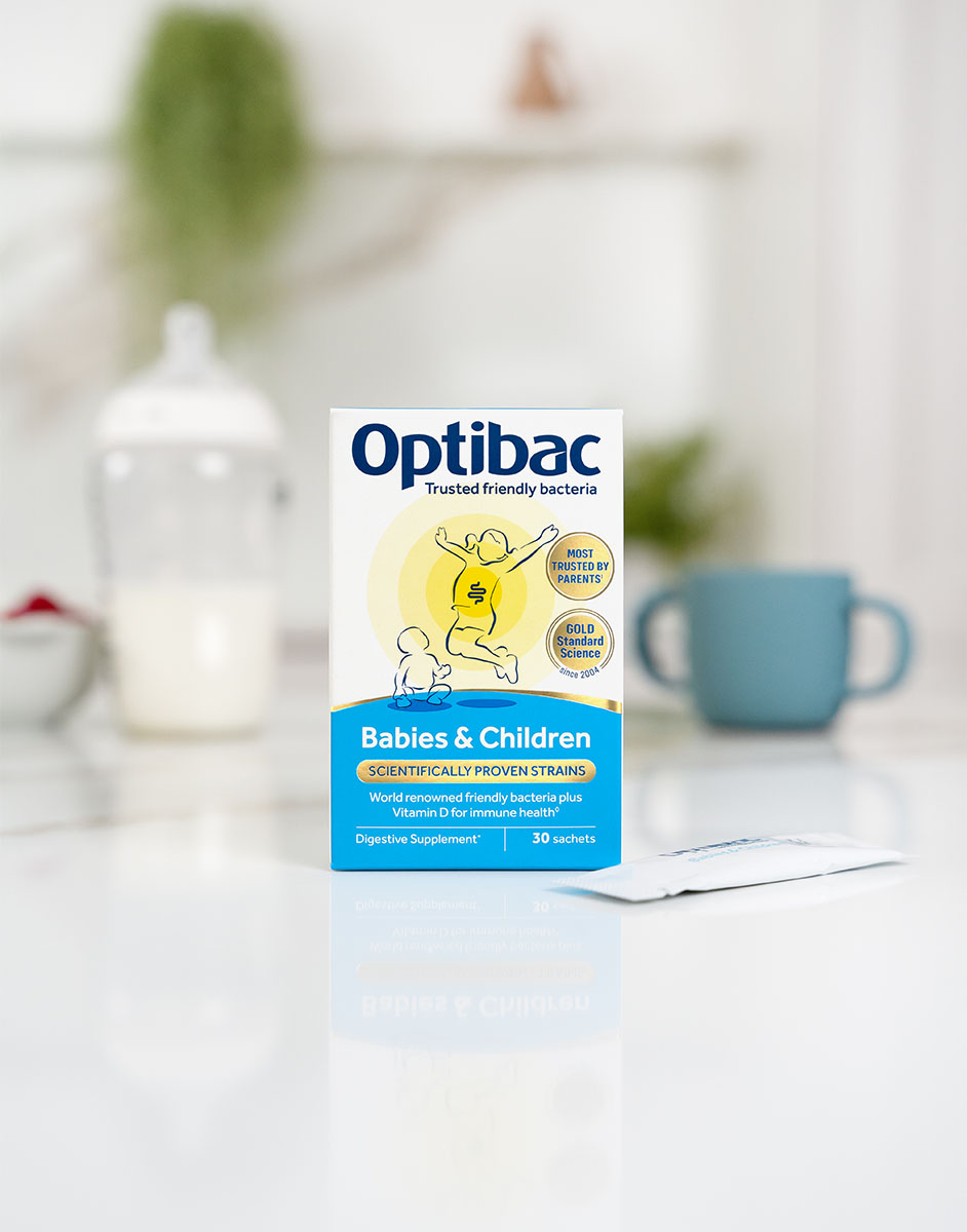 Box of Optibac probiotics for babies and children on a white surface, with a blurred kitchen background.