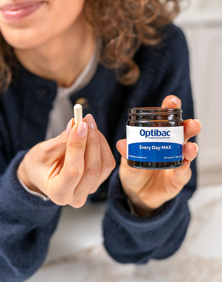 A person holds a capsule and an Optibac Every Day MAX supplement jar in a well-lit room.