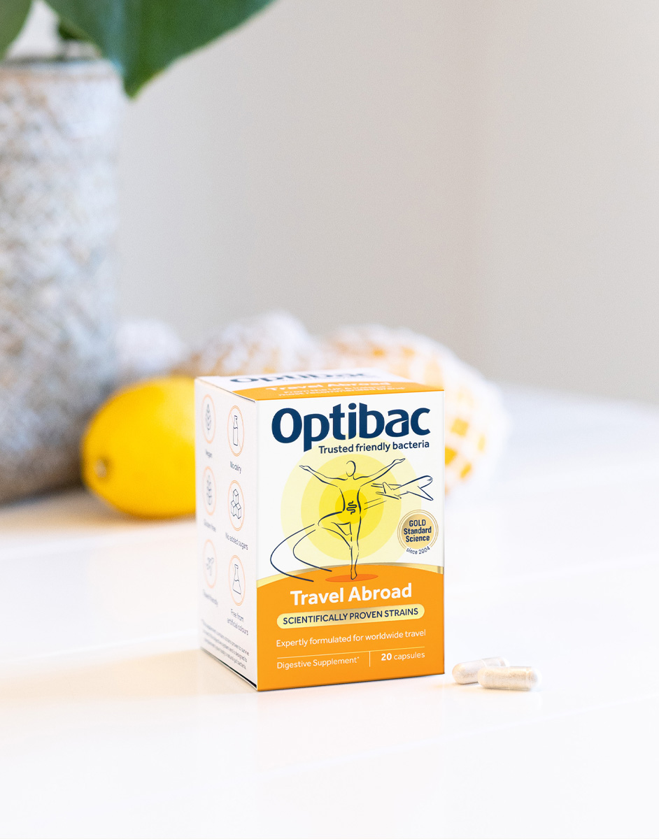 Box of Optibac Travel Abroad probiotics on a table with capsules beside it; lemons and a plant in the background.