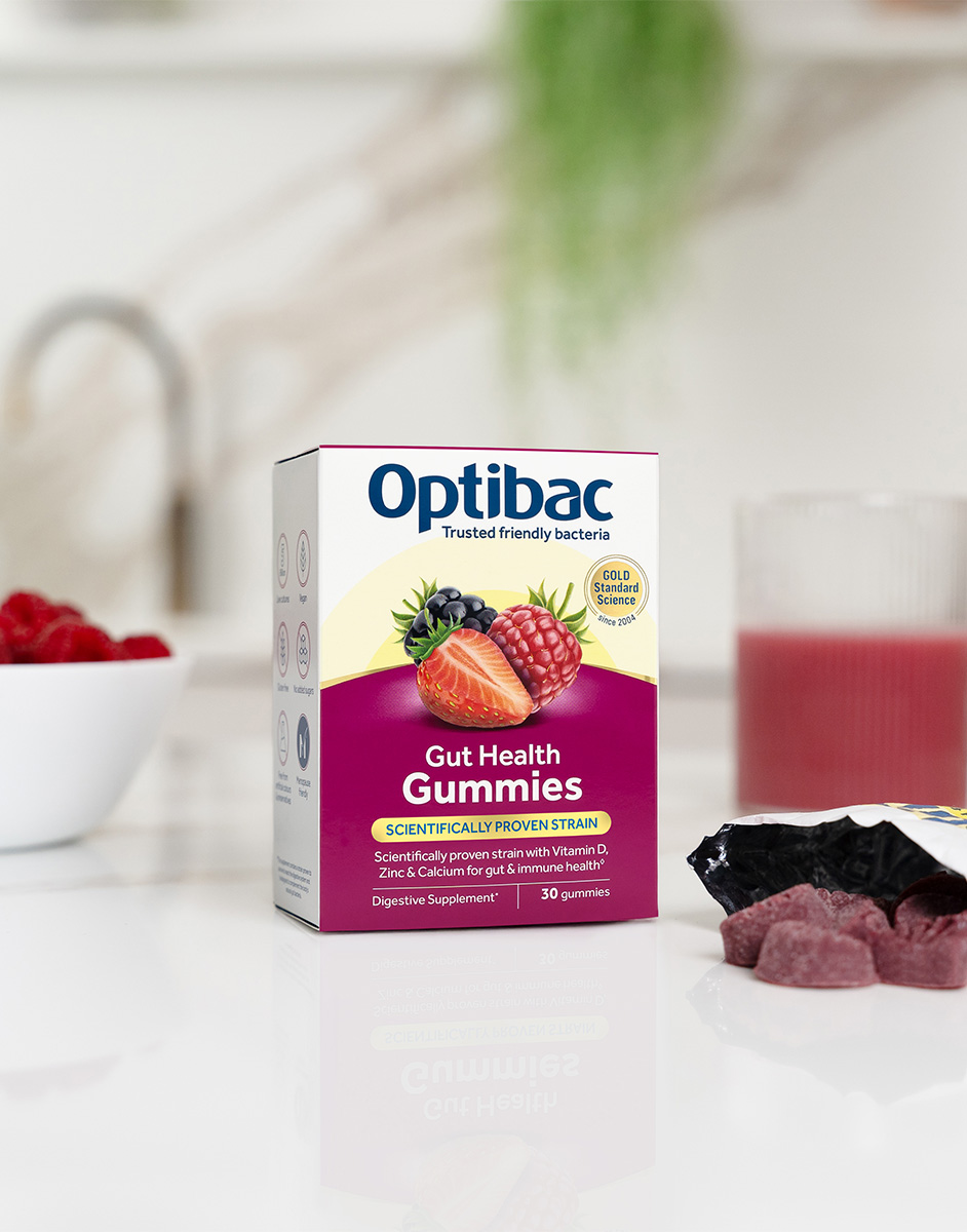 Box of Optibac Gut Health Gummies on a table with a glass of juice, fresh berries, and gummy pieces nearby.