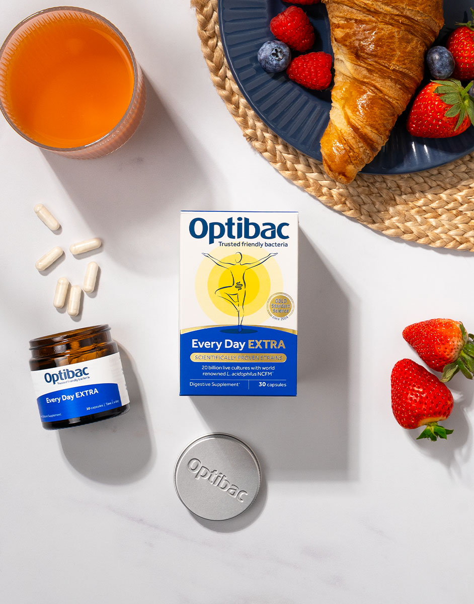 Optibac Every Day EXTRA capsules with a croissant, berries, and juice on a white surface.