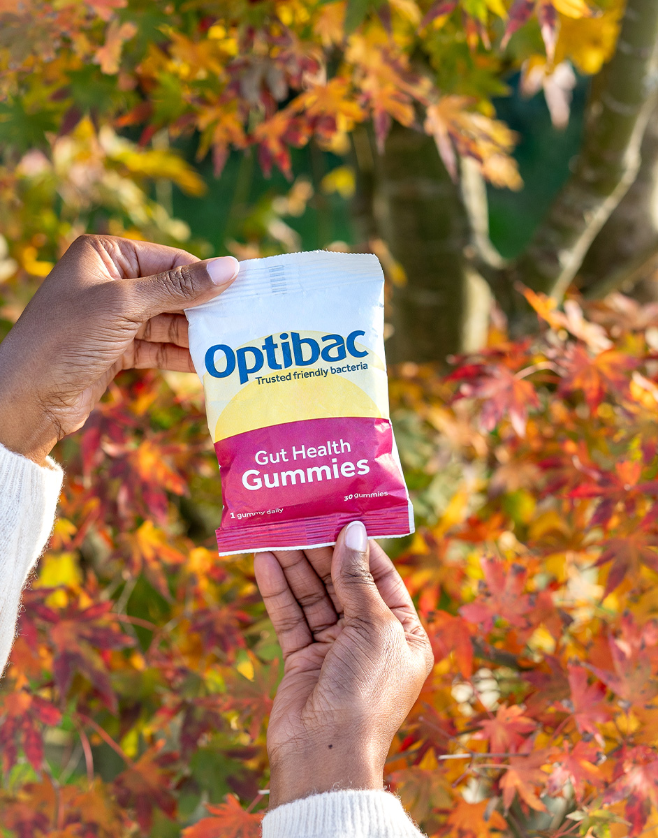 Hands holding a packet of Optibac Gut Health Gummies against a backdrop of autumn leaves.