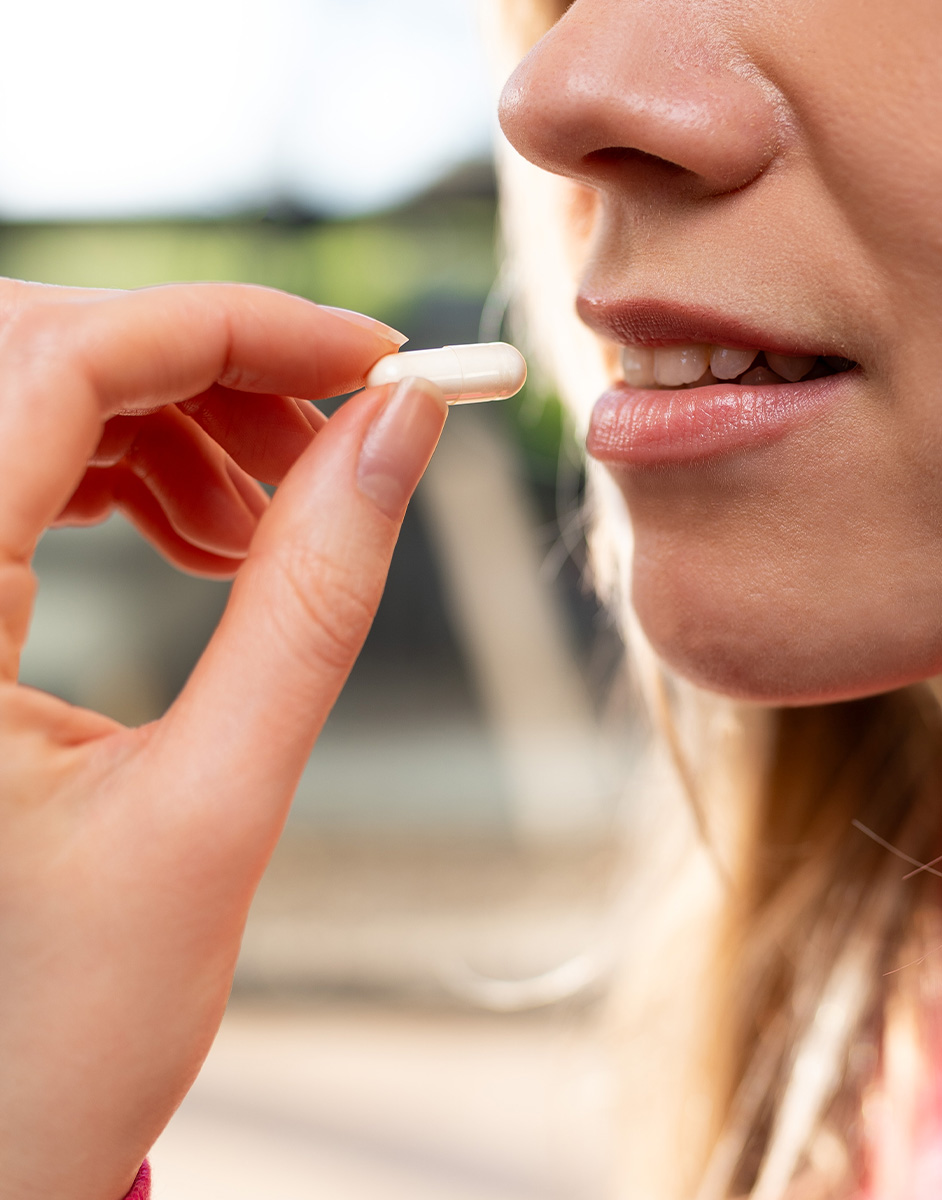 A person holding a white capsule near their lips, preparing to take it.