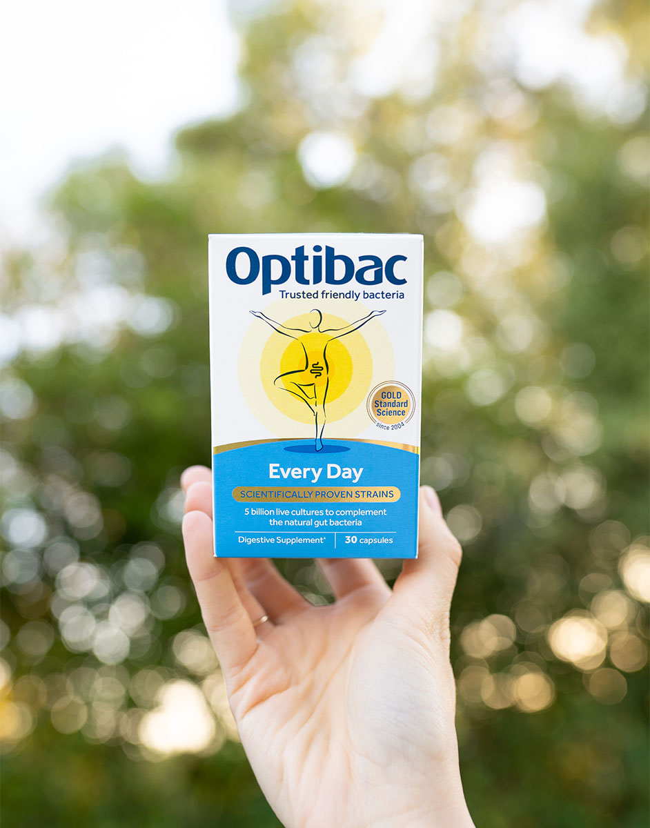 Hand holding a box of Optibac Every Day probiotic capsules against a blurred outdoor background.