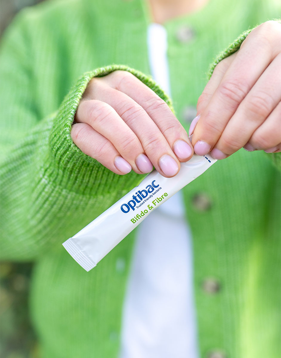 Person in a green sweater holding an Optibac sachet labeled "Bifido & Fibre" with both hands.