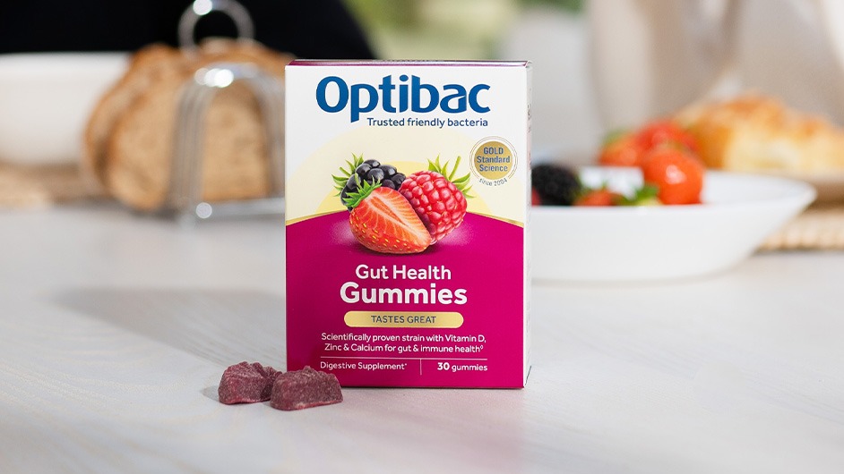 Box of Optibac Gut Health Gummies on a table, with fruit and breakfast items blurred in the background.