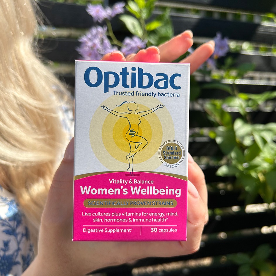 A person holds a box of Optibac Women's Wellbeing supplements outdoors, with text highlighting vitality, balance, and scientifically proven strains.
