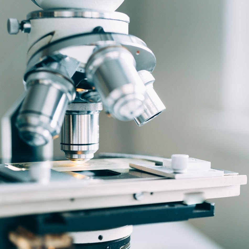 Close-up of a microscope with multiple objective lenses, focusing on a slide, in a bright laboratory setting.