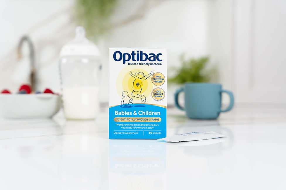 Optibac Babies & Children supplement box on a kitchen counter, surrounded by milk, a blue mug, and a bowl of berries.