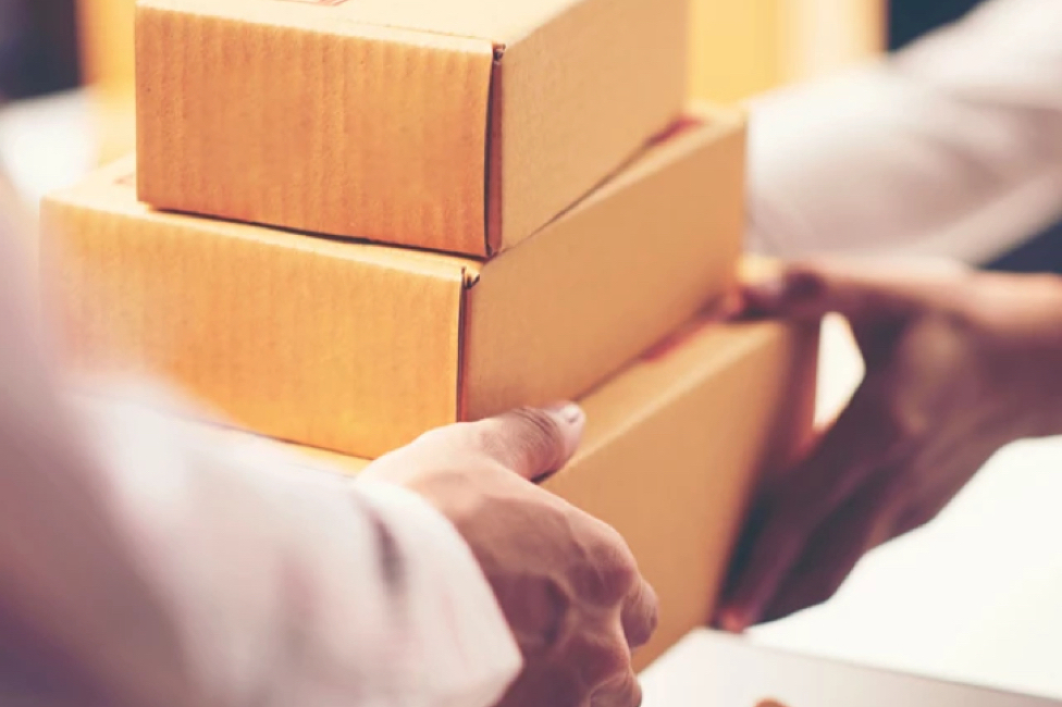 Two people exchanging a stack of cardboard boxes, suggesting a delivery or package handover.