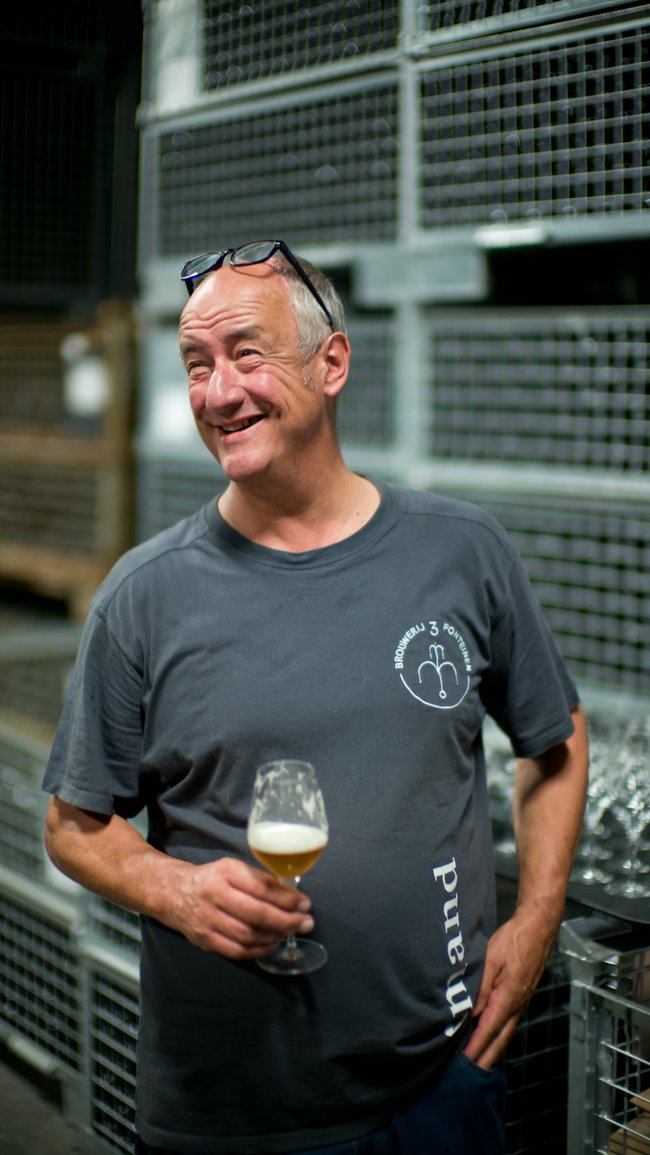 Portrait of Armand standing in the warehouse, holding a beer glass and smiling.