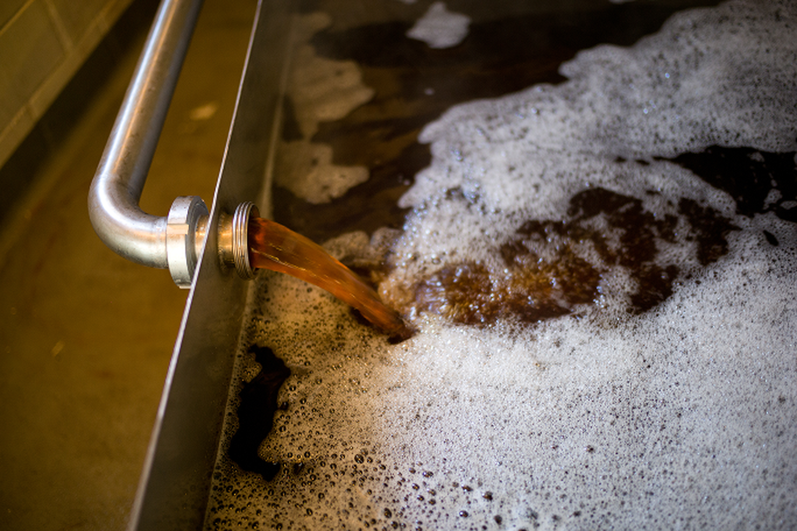 Steaming hot wort filling the large, shallow copper coolship (koelschip) in a dimly lit room filled with vapour.