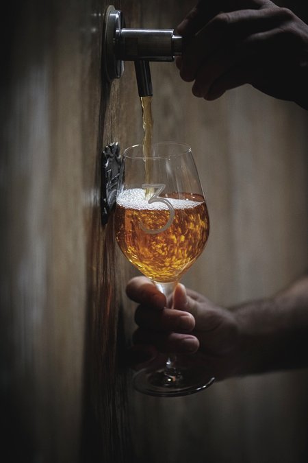 Een persoon schenkt donkerrode 3 Fonteinen Oude Kriek uit een 75cl fles in een glas op een houten tafel
