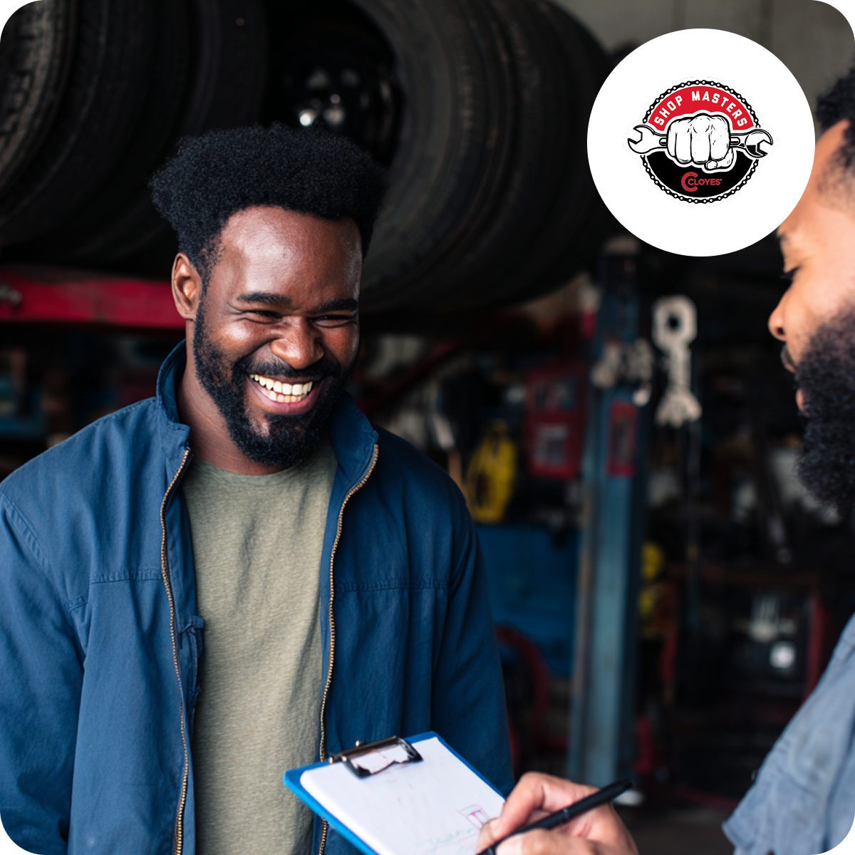 Two men in a garage smiling; one holds a clipboard. Shelves with tires are visible in the background. A "Shop Masters" logo is on the top right.