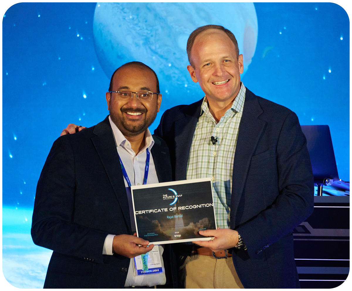 Two men smiling, holding a certificate of recognition on stage with a blue, planetary backdrop.