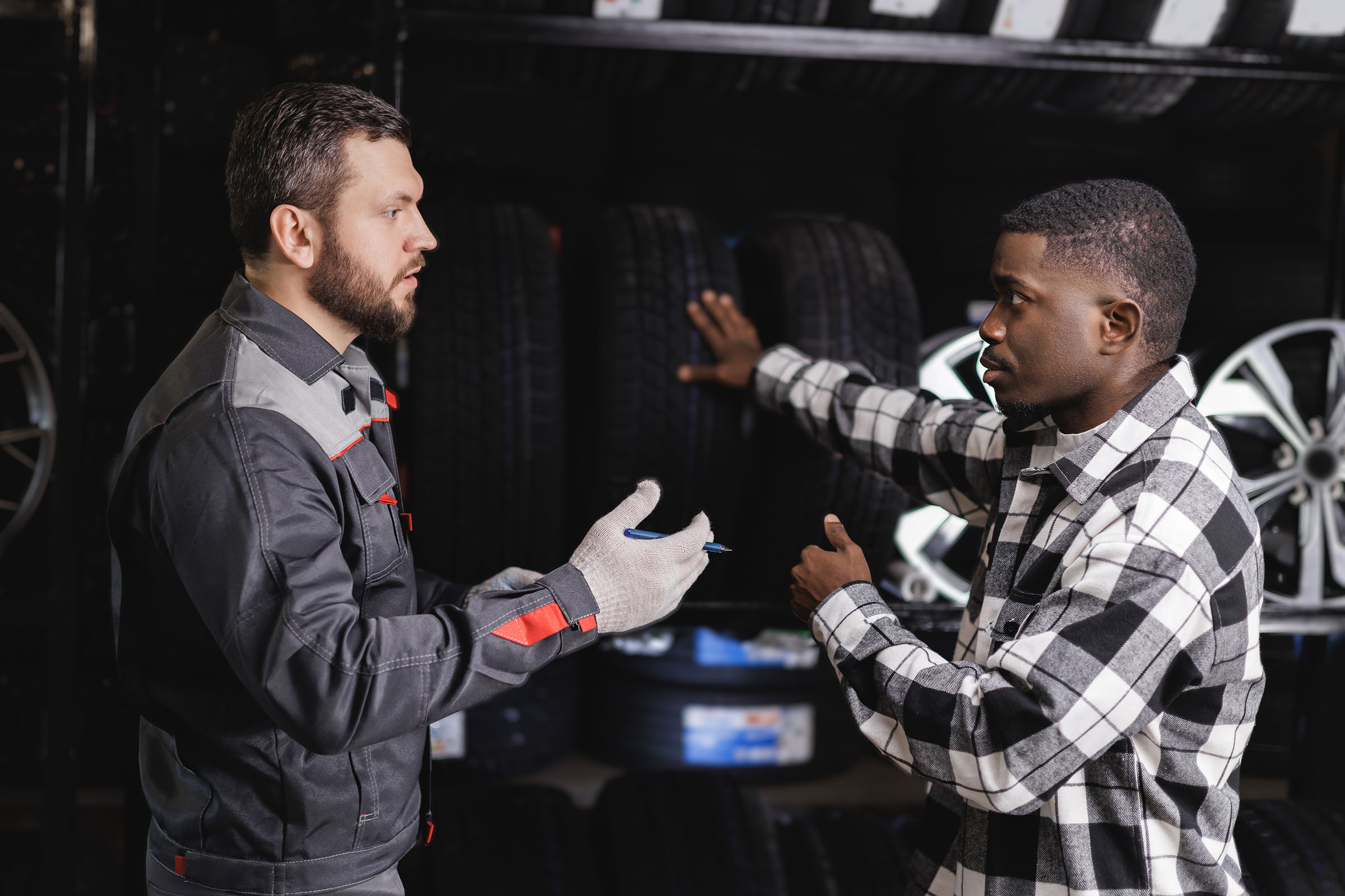 Customer and tire shop employee discussing tire options in front of a display of tires and rims.