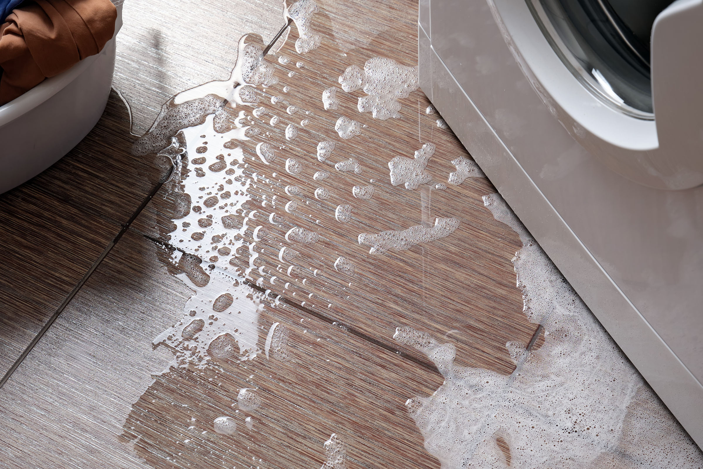 Soapy water spilled on the floor next to a front-loading washing machine, indicating a possible leak or overflow.